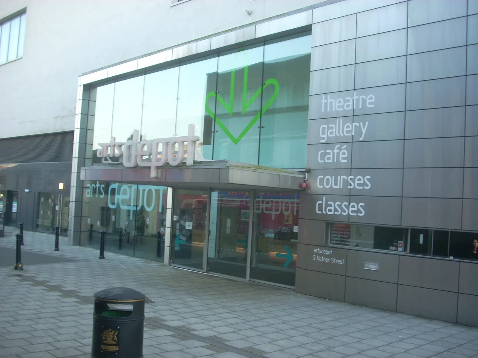 The artsdepot building entrance, with its name prominently displayed above the glass doors and a list of services like 'theatre' and 'gallery' on the adjacent wall.