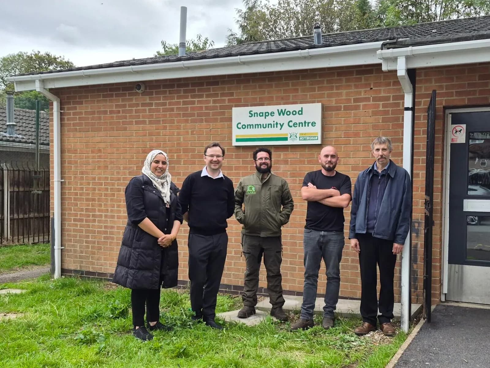 Five people stand outside a brick building with a sign that reads 'Snape Wood Community Centre'.